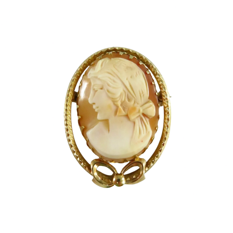 This vintage cameo brooch features a stunning profile of a woman, her hair adorned with a bow. The detailed carving is set in a 14k gold-filled prong setting. The outer edge of the oval frame boasts a lovely textured sawtooth design that gracefully curves into a bow at the bottom. This elegant cameo is in excellent condition and shows no signs of cracking