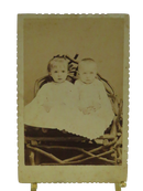 Antique photograph of two children in white dresses on a rustic chair