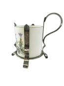 Silver-plated demitasse cup holder frame fitted around a white floral porcelain liner, showing a front support arm and scrolling loop handle.