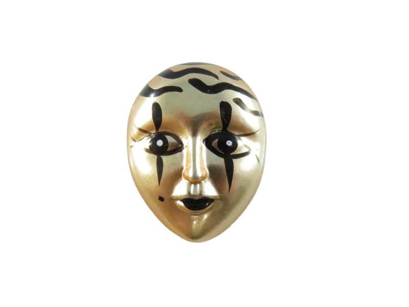 Gold mask-shaped brooch with black details on a white background