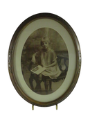 Front view of an oval framed sepia portrait photograph showing a young girl seated with an open picture book.