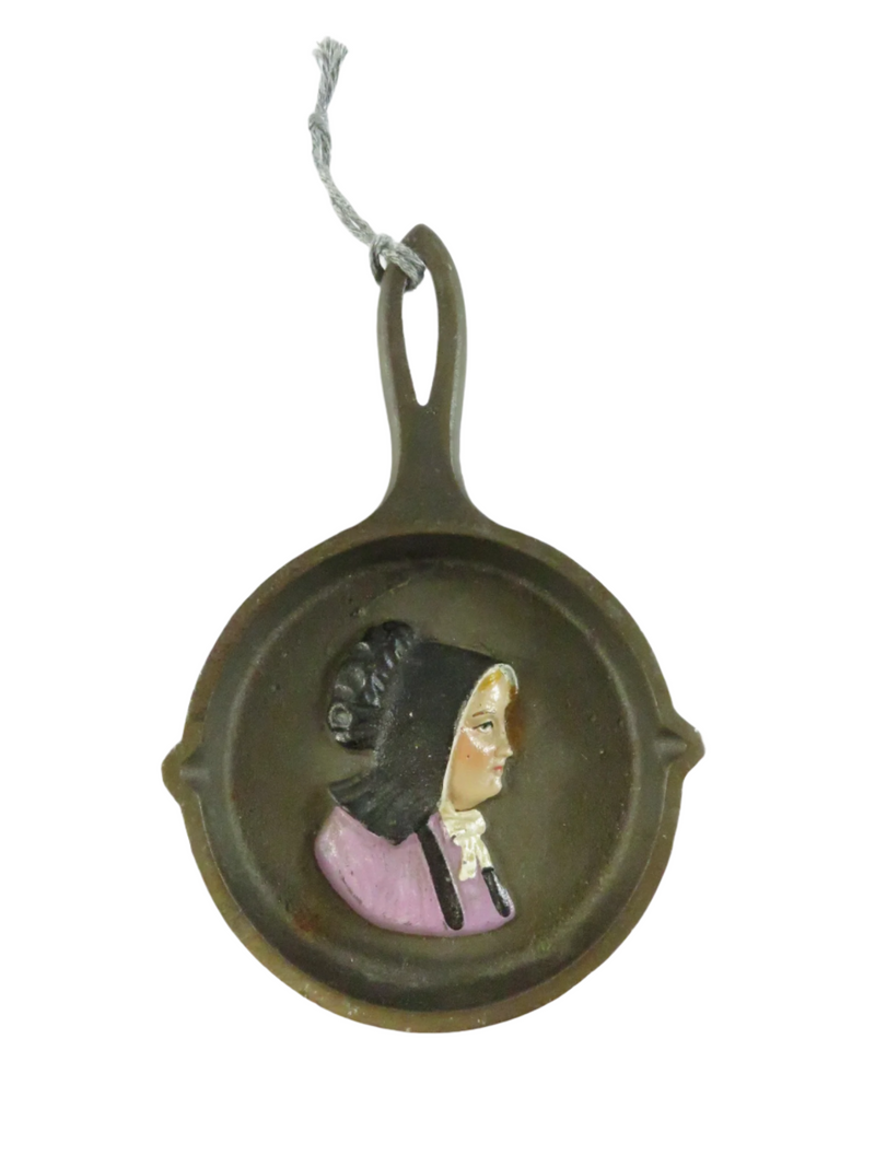Decorative ornament shaped like a miniature frying pan with a painted face on a white background