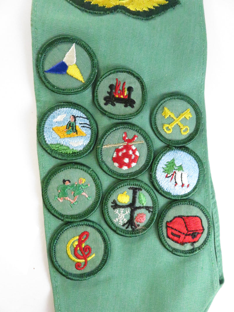 Green belt with various embroidered badges on a white background