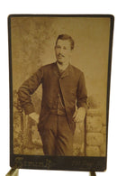 Man Leaning on Faux Stone Wall Antique Cabinet Card Strunk Reading PA — front view