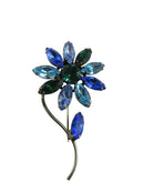 Floral brooch with blue and green gemstones on a white background