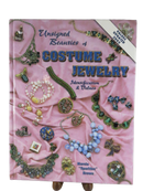 Front cover of Unsigned Beauties of Costume Jewelry by Marcia “Sparkles” Brown, showing assorted costume jewelry on pink fabric.