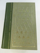 Close view of a green textured hardcover board with gilt border, diamond pattern, and floral motifs.