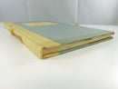 Low angled view of the hardcover showing the cream spine, blue-gray boards, page block, and worn glassine remnant.