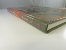 Low-angle view of the pictorial hardcover spine and fore-edge, showing the Rezazadeh spine lettering and worn lower corner.