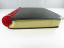 Low side view of the black flexible cover, red plastic comb, and age-toned text block.