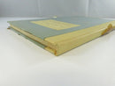 Rear cover view showing the blue-gray board, cream spine strip, and severely degraded amber glassine or cellophane wrap.