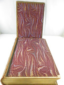 Opened leather volume showing marbled endpapers, exposed and damaged leather spine edge, and aged page edges.
